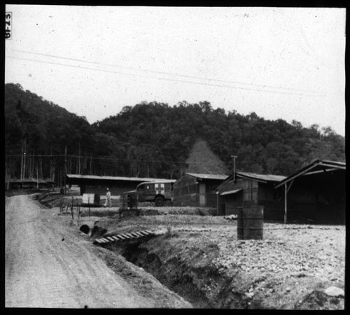 General view of road in hospital area showing ends of EENT, X-ray, and Surgery buildings to the left; end of ambulatory Officer Patient’s mess hall in the center; and Officer’s quarters to the right at the upper end of the road. Note gravel about clinic buildings, type of terracing, and necessary ditching with culvert and concrete 