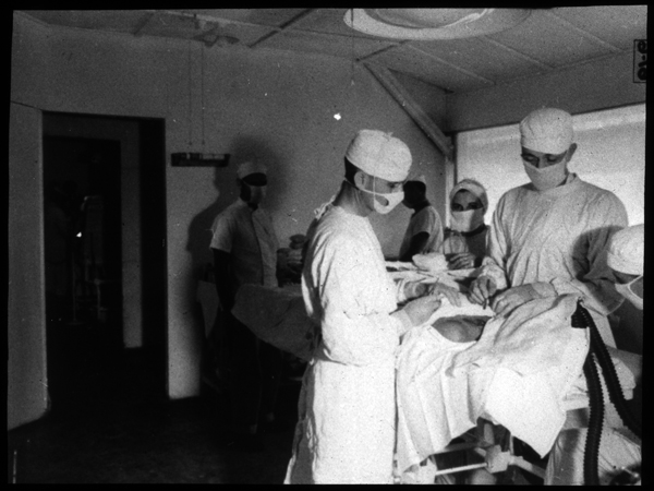 View of operating room in surgery building. Another operating room may be seen in background, with scrub room in between.