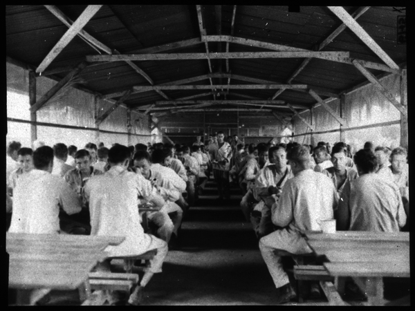 Interior view of ambulatory patients’ mess hall at meal time. Note screening on either side of hall, kitchen in background.