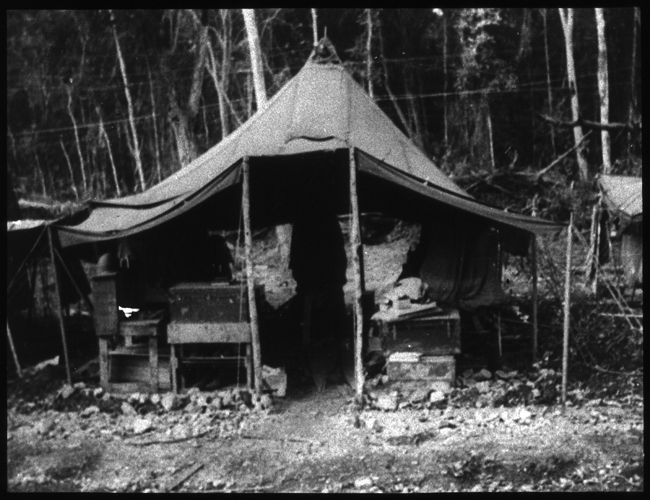 Exterior shot of an open tent as part of a row of tents, with various storage and chests underneath.